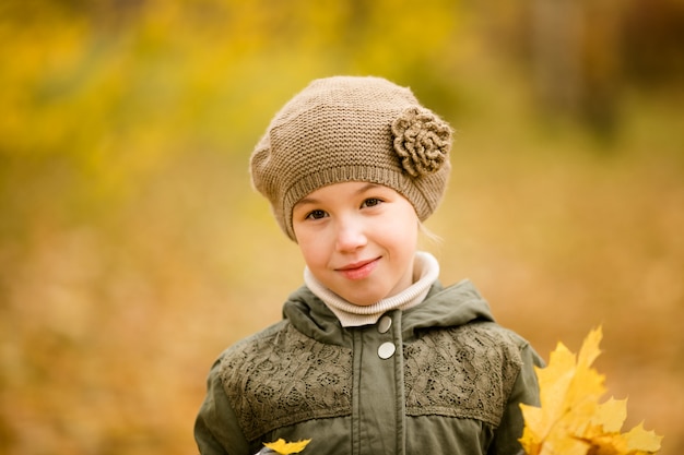 Nettes Mädchen im grünen Hut und im Mantel mit Gelb verlässt im Herbstpark