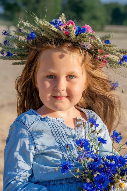 Nettes Mädchen im Vorschulalter mit einem Kranz auf dem Kopf und einem Strauß Wildblumen in den Händen. Glückliche Familie und freudige Kindheit