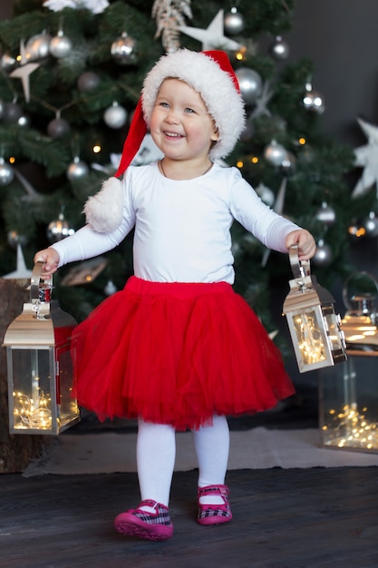 Nettes Mädchen in einem Hut des Weihnachtsmannes verbringt Zeit am Weihnachtsbaum