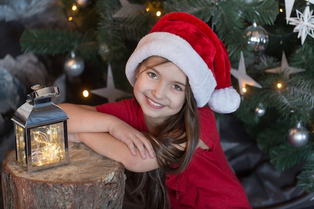 Nettes Mädchen in einem Hut des Weihnachtsmannes verbringt Zeit am Weihnachtsbaum