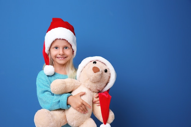 Nettes Mädchen in Weihnachtsmütze mit Spielzeug auf farbigem Hintergrund