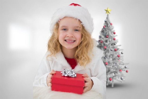 Nettes Mädchen mit Geschenk gegen Weihnachtsbaum im hellen Raum