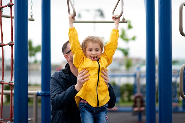 Nettes Mädchen mit ihrem Vater auf dem Sportplatz Mädchen versucht, an Sportsimulatoren zu trainieren und hat Spaß