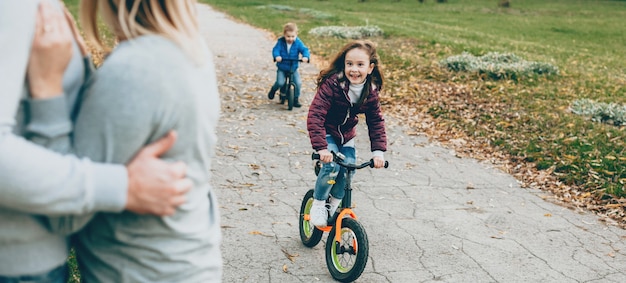 Nettes Mädchen mit kleinem Bruder, der das Fahrrad im Park reitet, während Eltern sie beobachten