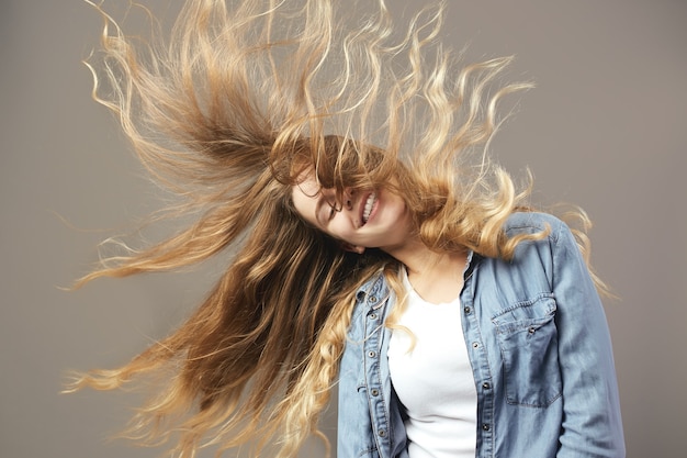 Nettes Mädchen mit langen braunen, fließenden Haaren lächelt auf grauem Hintergrund.