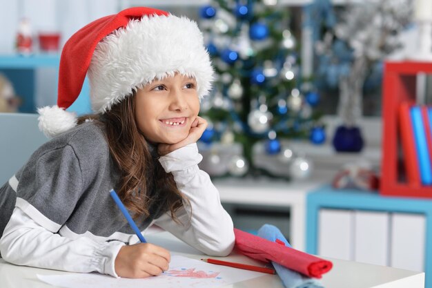 Nettes Mädchen mit Weihnachtsmütze, das Brief schreibt