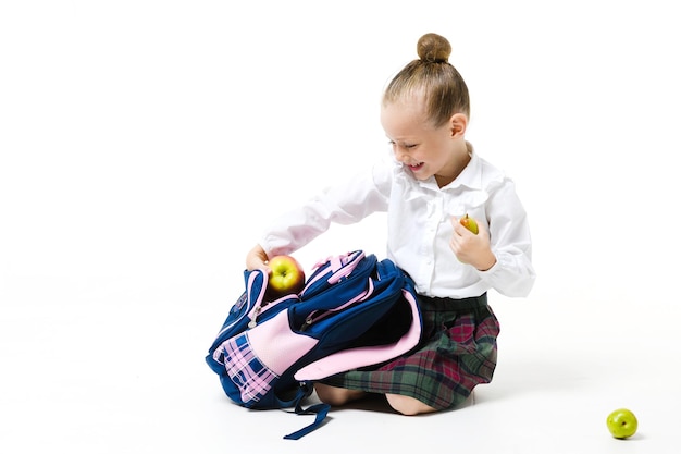 Nettes Mädchen sammelt einen Rucksack für den Unterricht isoliert auf weißem Hintergrund