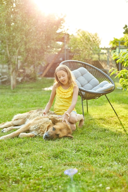 Nettes Mädchen und alter Hund genießen den Sommertag auf dem Gras im Park