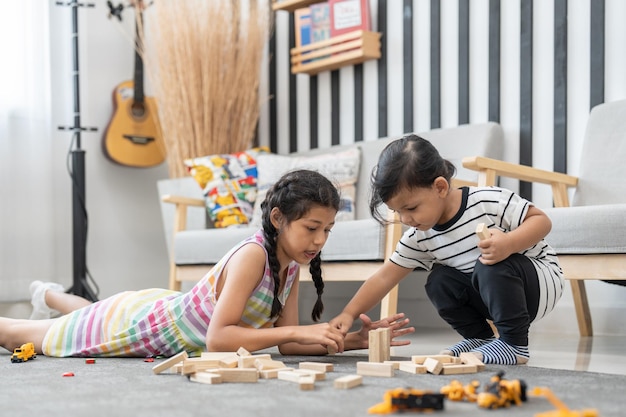 Nettes Mädchen und kleiner Junge spielen Holzblockstapelspiel auf dem Boden im Wohnzimmer zu Hause