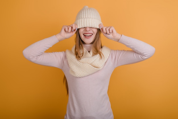 Nettes Mädchen zog einen beige Hut über ihre Augen und lacht auf einem orange Hintergrund, Winter, neues Jahr