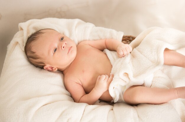 Nettes nacktes kaukasisches Baby, das unter einer Decke auf dem Bett liegt