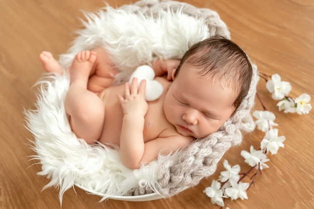 Nettes neugeborenes baby 0-14 tage, die in einem kinderbett mit blumen schlafen. vorlage zum verpacken von kinderprodukten. nahaufnahmeporträt eines neugeborenen babys mit einem lächeln auf seinem gesicht.