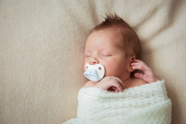 Nettes Neugeborenes Baby, das auf weißer Decke mit einem Schnuller schläft