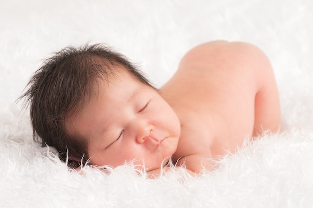 Nettes neugeborenes Baby, das mit dem Gesicht nach unten auf einem weichen, weißen, flauschigen Tuch schläft.