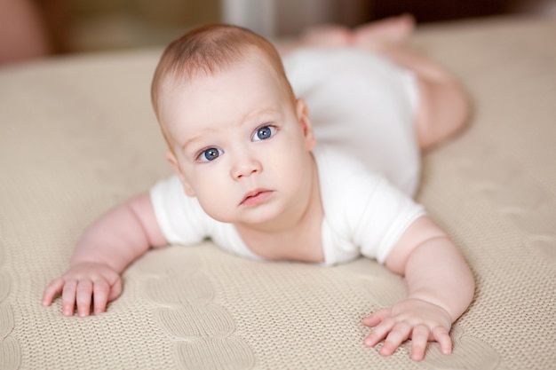 Nettes schönes Baby mit großen Augen liegt auf dem Bett