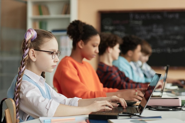 Nettes Schulmädchen, das Computer in Reihe im Klassenzimmer benutzt