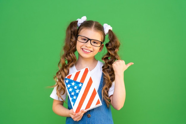 Nettes Schulmädchen mit einem Lehrbuch und einem Bild der amerikanischen Flagge. Ein charmantes Mädchen zeigt auf Ihre Anzeige.