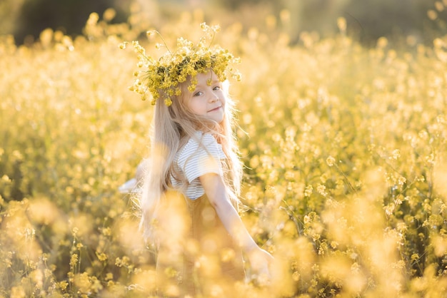 Nettes stilvolles Kindermädchen tragen Blumenkranzständer in der gelben Blumenwiese im Freien über der Natur