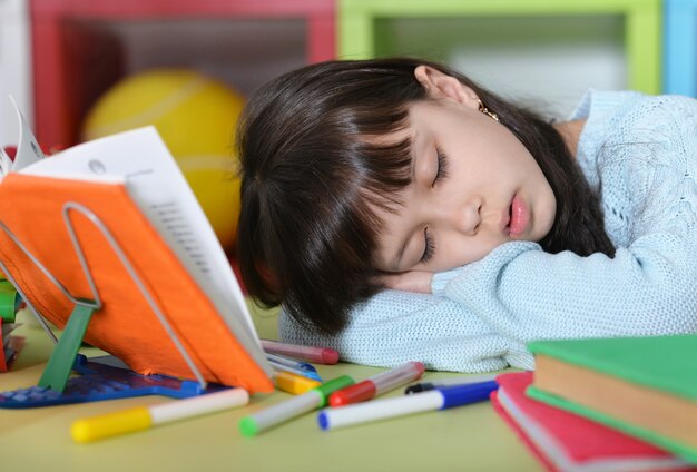 Nettes Studentenmädchen, das im Unterricht in der Nähe von Büchern schläft