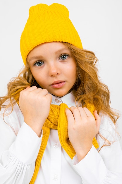 Nettes Teenager-Mädchen in einem gelben Hut mit einem Schal auf weißer Nahaufnahme