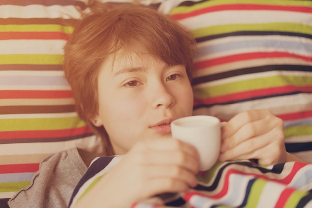 Nettes Teenagermädchen, das mit einer Tasse Kaffee in der Hand im Bett liegt Getönt