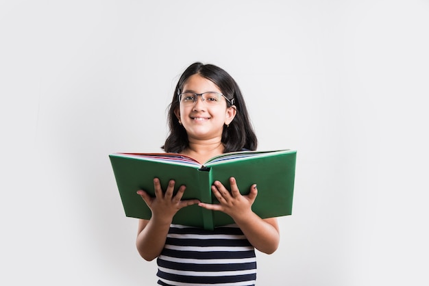 Nettes und fleißiges kleines indisches oder asiatisches Mädchen, das ein Buch hält oder studiert oder liest, während es auf weißem Hintergrund steht