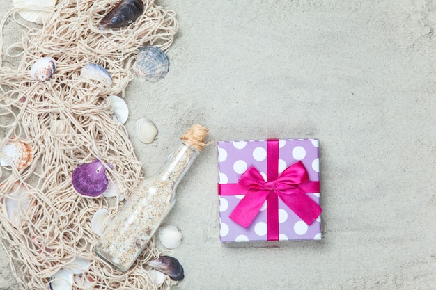 Netz, Muscheln mit Flasche und Geschenkbox auf Sand.