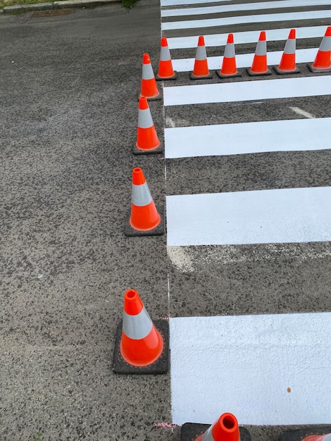 Neu gestrichene gestreifte Fahrbahnmarkierungen eines Fußgängerüberwegs sind mit Leitkegeln eingezäunt.