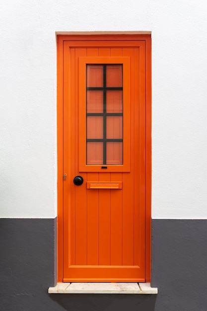 Neue geschlossene moderne leuchtend orangefarbene Tür in einer weißgrauen Wand