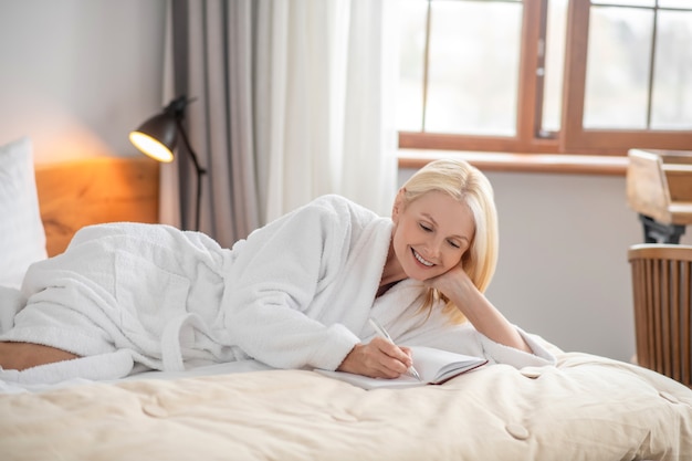 Neue Ideen. Eine süße Frau, die auf dem Bett liegt und Notizen macht