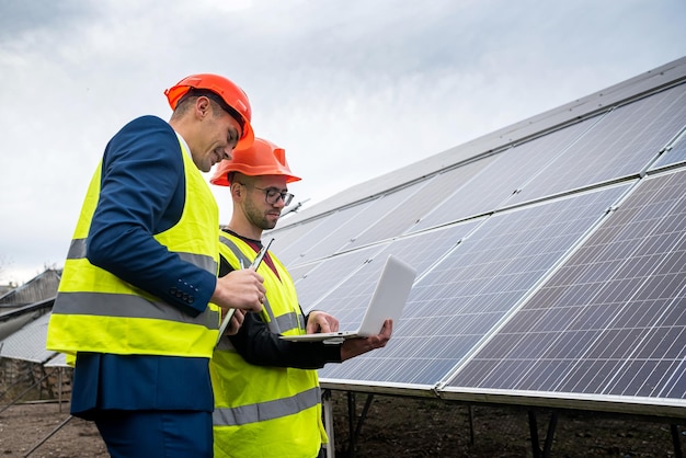 Neue junge Berufstätige in Berufshelmen und Spezialkleidung diskutieren über einen Plan zur Installation von Sonnenkollektoren Das Konzept der Installation von Ökostrom