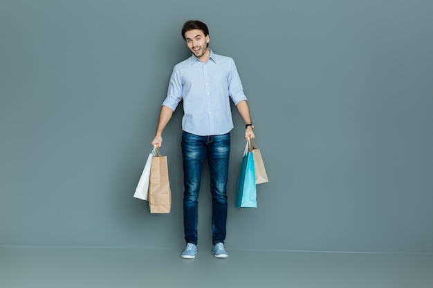 Neue Kleidung. Netter fröhlicher positiver Mann, der lächelt und Taschen beim Einkaufen hält