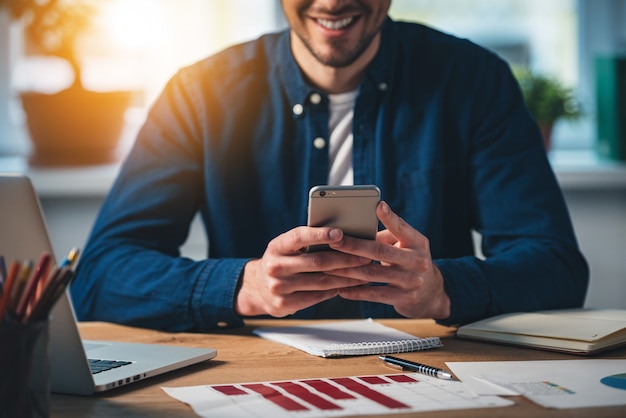 Neue Nachricht! Nahaufnahme eines fröhlichen jungen Mannes, der sein Smartphone mit einem Lächeln verwendet