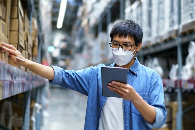 Neue normale asiatische Männer, Mitarbeiter, Produkt mit Gesichtsmaske. Zählen Warehouse Control Manager Stehen, Zählen und Prüfen von Produkten im Lager