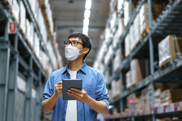 Neue normale asiatische Männer, Mitarbeiter, Produkt mit Gesichtsmaske. Zählen Warehouse Control Manager Stehen, Zählen und Prüfen von Produkten im Lager