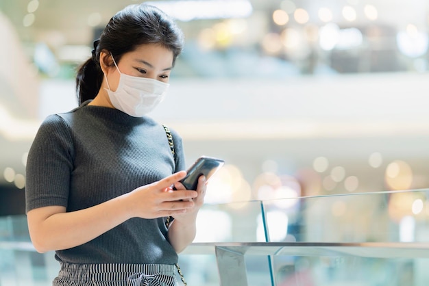 Neue Normalität nach Covid19-Epidemie Smart asiatische Frauen tragen Schutzmaske Hand verwenden Smartphone-Kommunikation im Kaufhaus neuer Lebensstil abstrakter unscharfer Hintergrund