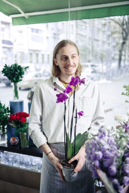 Neue Sorte. Fröhlicher Florist, der ein Lächeln auf seinem Gesicht behält und zur Seite schaut