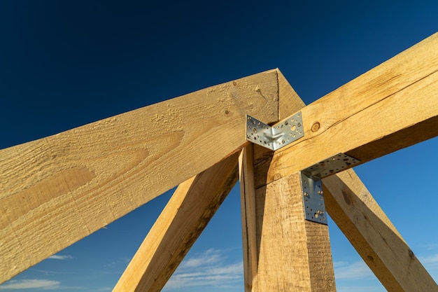 Neue Wohnungsbaurahmen und Installation von Holzbalken am Dachstuhlsystem des Hauses vor blauem Himmel