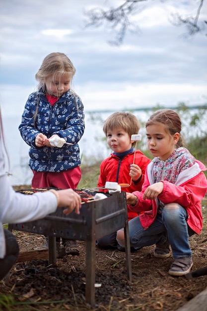 Neuer normaler Fluchtschritt, wildes Wandern in der Natur und Erholung mit der Familie im Freien. Kinder am Feuer stehen und Marshmallows kochen, am Wochenende wandern, Lebensstil