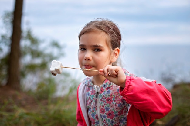 Neuer normaler Fluchtschritt, wildes Wandern in der Natur und Erholung mit der Familie im Freien. Kinder kochen und probieren Marshmallows, die am Feuer gebraten werden, wandern am Wochenende, Lebensstil