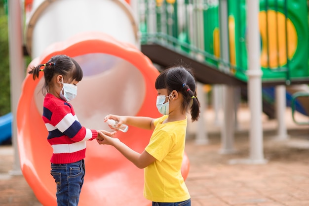 Neuer normaler Lebensstil, Konzept der sozialen Distanzierung. glückliche Kinder mit Gesichtsmaske, die sich auf dem Spielplatz amüsieren, schützen das Coronavirus Covid-19,