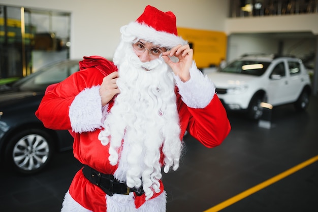 Neues Auto als Weihnachtsgeschenk. Weihnachtsmann im Autohaus in der Nähe eines Neuwagens.