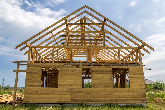 Neues Häuschen aus natürlichen ökologischen Holzmaterialien im Bau auf der grünen Wiese. Holzwände und steiler Dachrahmen.