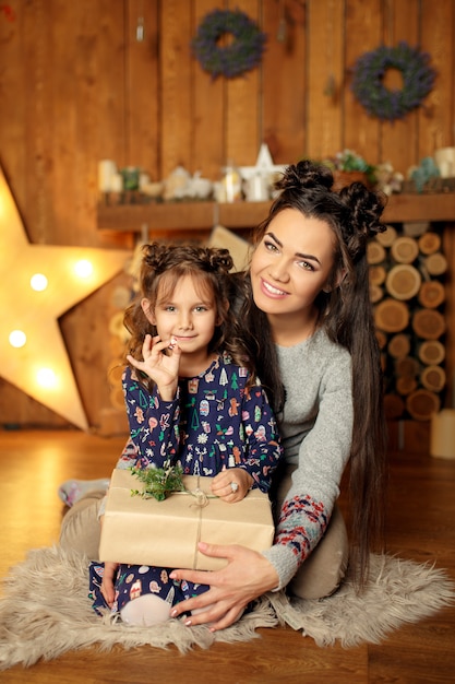 Neues jahr 2020. frohe weihnachten, schöne feiertage. nahaufnahmeporträt eines kleinen mädchens mit mama und geschenkbox. magisches licht im nachtweihnachtsbaum-innenraum