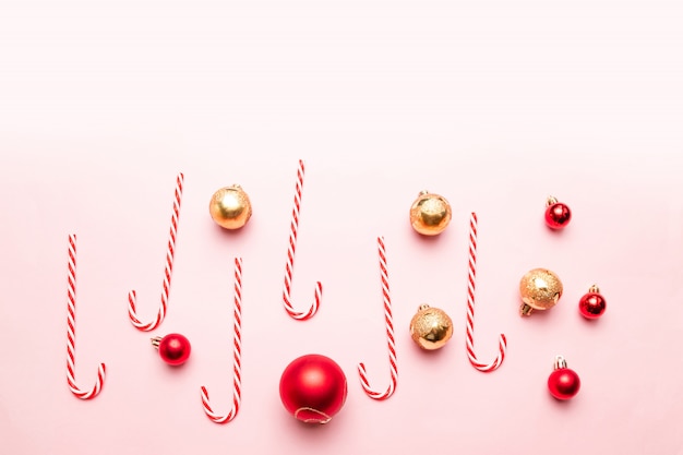 Neues Jahr-Weihnachten mit Zuckerstangen, Gold und roten Bällen auf rosa Hintergrund. Flache lage, draufsicht, copyspace