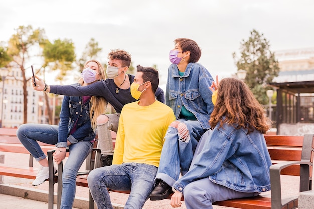 Neues normales Corona-Virus-Leben mit einer gemischtrassigen Gruppe junger Studenten, die ein Selfie mit Gesichtsmaske macht