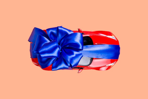 Neues rotes Auto mit einem blauen Bogen als Geschenk auf Koralle