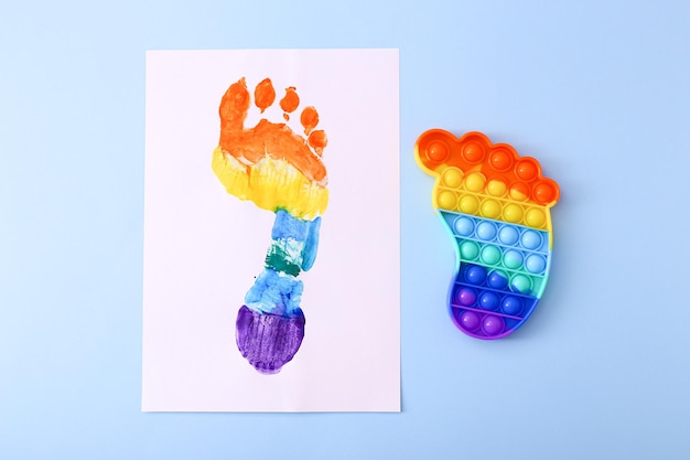 Neues trendiges beliebtes Silikon buntes Anti-Stress-Pop-It-Spielzeug für Kinder und bunte Fußabdrücke auf blauem Hintergrund.