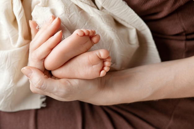 Neugeborene Babybeine in der Handfläche der Mutter schließen. Mutterschafts-, Familien-, Geburtskonzept.