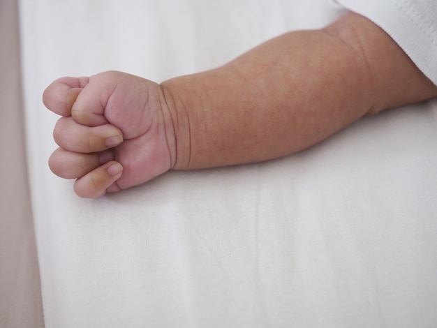 Neugeborene Babyhand auf weißem Bett